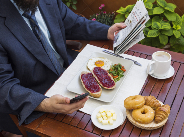man-holding-smartphone-newspaper-during-breakfast